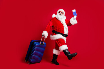 Full length photo of retired old man white beard hold suitcase tickets passport check-in airport wear x-mas santa costume glove coat belt sunglass cap boot isolated red color background
