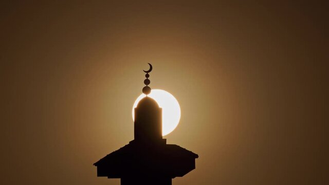 Sun setting down behind a silhouette of a mosque minaret in Doha, Qatar.
