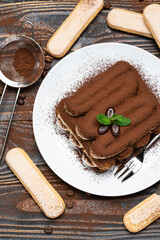 Classic tiramisu dessert on ceramic plate and savoiardi cookies on wooden background