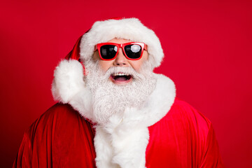 Closeup portrait photo of retired old man grey beard open mouth cheerful smiling make wish newyear eve family holiday wear santa costume sunglass headwear isolated red color background