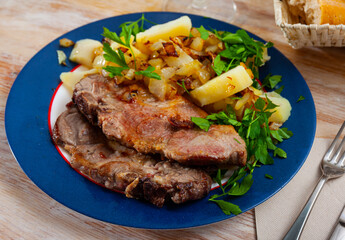 Close up of delicious baked pork with potatoes and greens, served on plate..