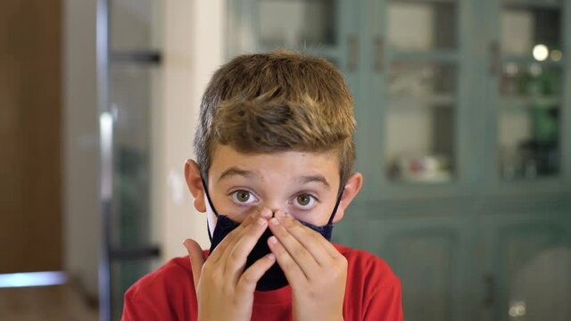 Caucasian boy puts on a protective mask at home looking at camera. Concept new rules, new normality during Coronavirus, COVID-19.