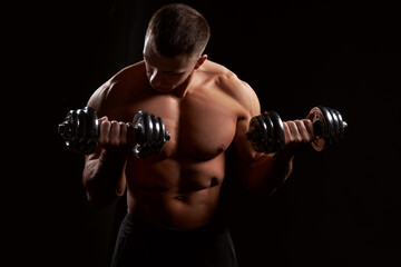 Fototapeta na wymiar Shirtless muscular man holding dumbbells against of black background.Studio shot