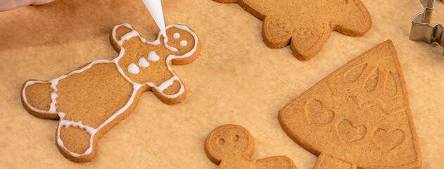 Young woman is decorating Christmas Gingerbread House cookies biscuit at home with frosting topping in icing bag, close up, lifestyle.