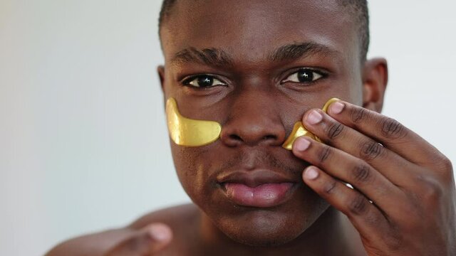 Man skincare. Facial treatment. Portrait of annoyed black guy trying to apply gold hydrogel eye patches disappointed failing isolated on light background. Metrosexual lifestyle. Anti-aging procedure.
