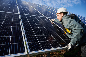 Professional worker, wearing protective suit, helmet and gloves, installing a photovoltaic solar batteries on a sunny day. Concept of alternative energy and power sustainable resources.