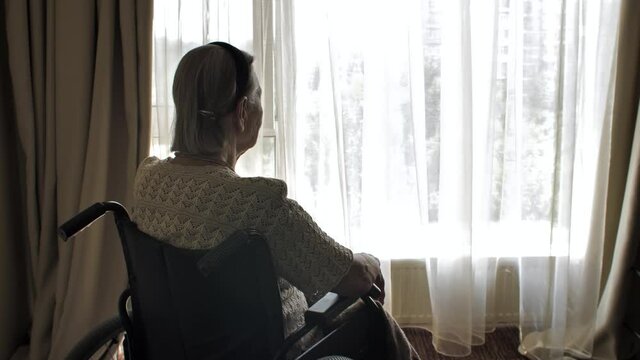 Disabled woman sit on wheelchair and looks through the window