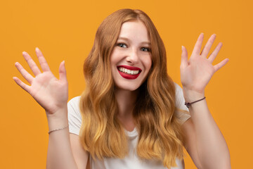 Positive Young woman with long wavy blonde hair, wearing white t-shirt smiling happily and spreads her hands to the side