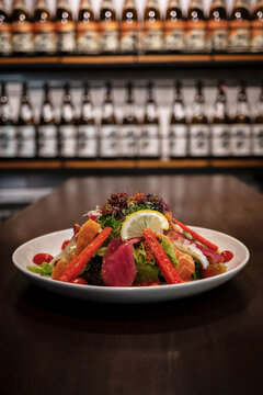 Close-up of Japanese food mixed Sashimi salad dish on wood table with blurred sake bottles rows on shef background, thinly sliced raw fish seafood with spicy seasoning, lemon and vegetables salad.