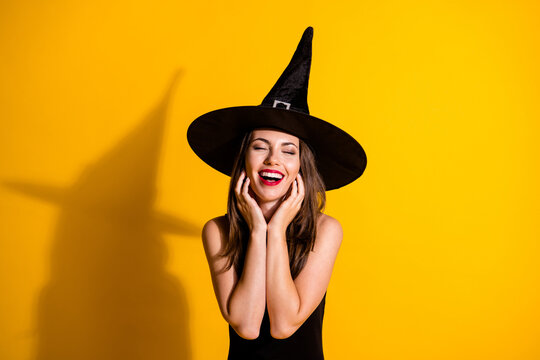 Photo of cute pretty young lady eyes closed open mouth hands face hear flattery complimented fall theme event wear black witch costume cone headwear isolated yellow color background