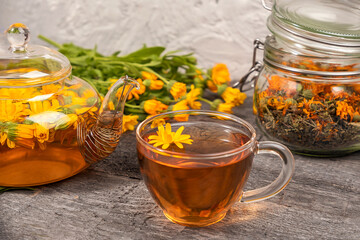 Cup of herbal tea, transparent teapot and marigold flowers on wood background. Calendula Tea Benefits Your Health concept. Front view.