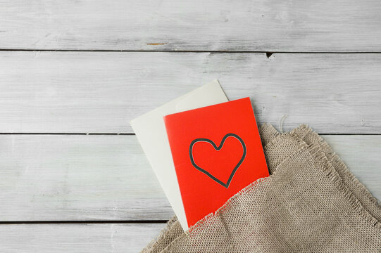 red paper card with heart and white envelope on rough cloth on light wooden table. holiday image for lovers