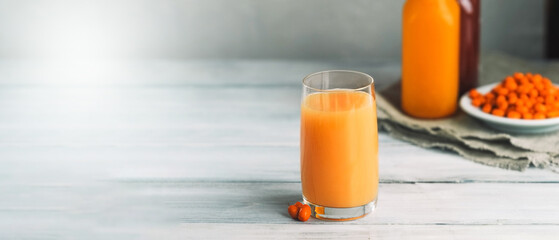 glass of orange juice and two clear bottles of orange detox drink, plate full of ripe sea buckthorn berries on the background. Banner about healthy eating and weight loss