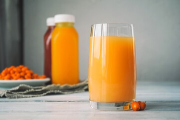 glass with bright highlights of orange juice and two clear bottles of orange detox drink, plate full of ripe sea buckthorn berries on the background. Banner about healthy eating and weight loss