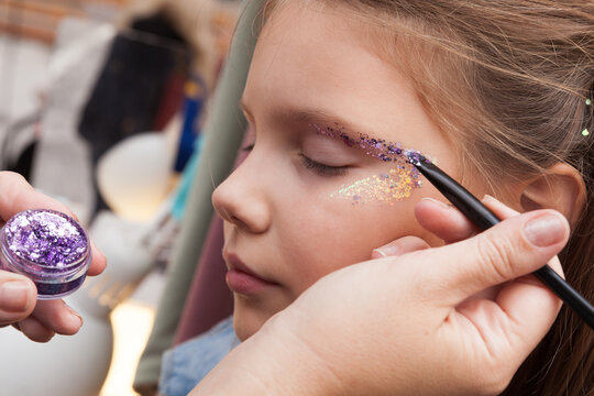Little European girl face makeup applying with glitter