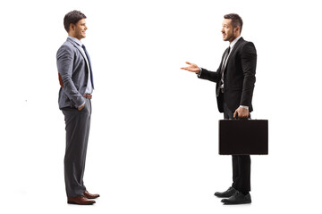 Full length profile shot of a businessman in a suit with a briefcase talking to a man