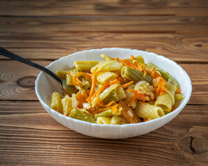 Lunch with pasta and vegetables in a deep white plate with a fork close-up on table
