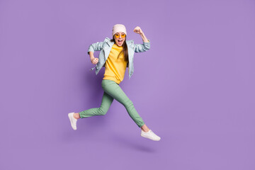 Full size profile side photo of amazed excited girl enjoy lottery discount win jump run fast speed wear green pants headwear sunglass isolated over violet color background