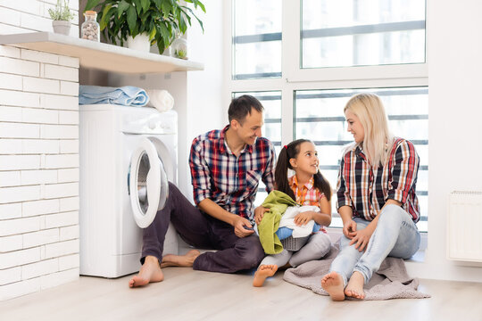 family mother, father and child girl little helper in laundry room near washing machine and dirty clothes