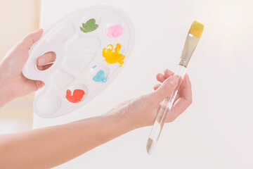 Woman artist holding palette with different paints and paintbrush