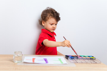 The kid paints at the table with paints on a piece of paper. Classes with your child at home. Preschool development at home