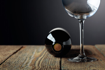 Unopened bottle of red wine and empty wine glass on an old wooden table.