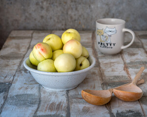 White nectarines in a deep ceramic plate, a mug and two wooden boats on a rustic table
