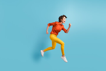 Full length profile photo of attractive pretty funny lady rushing shopping center sales running fast speed excited wear orange shirt yellow trousers sneakers isolated blue color background