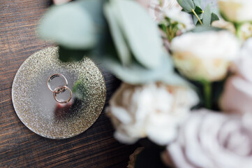 beautiful gold wedding rings on wood floor next to bouquet and shoes