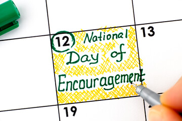 Woman fingers with pen writing reminder National Day of Encouragement in calendar.