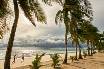 Young couple walking along the clean White Beach with coconut trees at sunset with cloudy sky at Boracay Island, Aklan Province, Visayas, Philippines