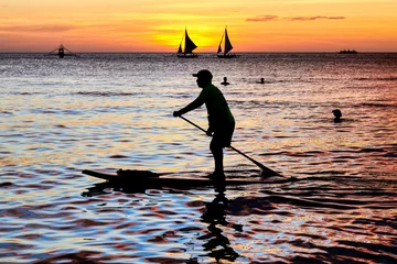 Photo sur Plexiglas Plage blanche de Boracay La silhouette d& 39 un homme sur un paddle board, des gens nageant et deux voiliers au coucher du soleil le long de la plage blanche sur l& 39 île de Boracay, Aklan, Philippines.