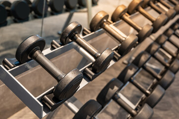 Group of black metal dumbbells on rack in exercise gym. Weight training equipment in sport fitness centre. Muscle building workout concept