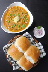 Indian Mumbai Street style Pav Bhaji, garnished with peas, raw onions, coriander and Butter. Spicy thick curry made of out mixed vegetables, served with paav over black background with copy space. 