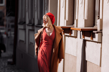 stylish blonde in a red dress in the spring city. Beautiful girl in red dress posing on city streets. Stunning young woman walking in the city.