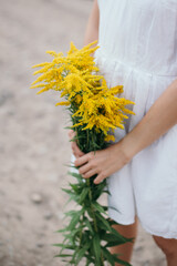 Girl in a white linen dress with a bouquet of yellow wildflowers.