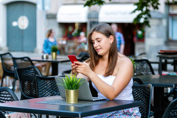young woman work on laptop and using phone sitting in street cafe, tistance learning and work concept