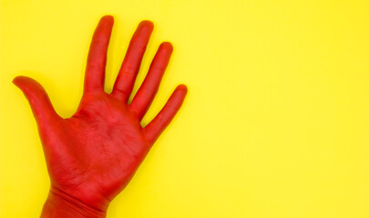 top view of red painted hand with open palm on yellow background with space for text
