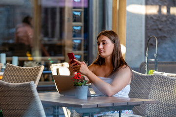 young woman work on laptop and using phone sitting in street cafe, tistance learning and work concept