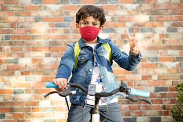 Caucasian boy on his bike ready to go to school. He wears a face mask. Concept of return to school and new normal.