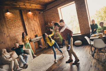 Photo of full big family eight people gathering two little kids play dad piggyback grandparents sitting sofa dinner table drink wine talk generation in home evening living room indoors