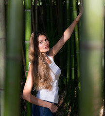 Fototapeta na wymiar Blonde with long hair in a bamboo forest. Girl in a white t-shirt in a tropical garden