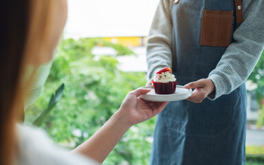 A waitress holding and serving a piece of red velvet cupcake to customer