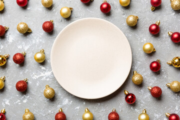 Naklejka na ściany i meble Top view of festive plate with red and golden baubles on cement background. Christmas decorations and toys. New Year advent concept