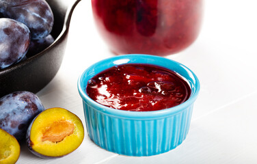 Homemade damson plum jam in blue ceramic bowl and berries on white wooden background.
