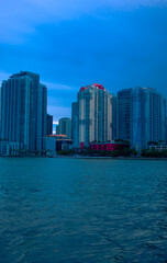 View of buildings in Brickell Miami, Florida as night time nears, High rises near water in Miami, Cold look of buildings, Cold look of high rises, Cold look of buildings near water, Nighttime in city