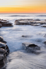 Ocean water flow between rocks during dawn at Coalcliff Beach, Australia.