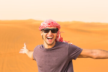 Happy young male tourist having fun enjoying a safari trip in the Arabian desert sand dunes wearing a local headwear. Travel and tourism. 