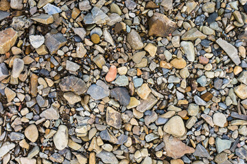 The texture of small river stones. Brown, yellow, blue and blue colors. Background with space for text. Camping. Bank of the river, sea, ocean.