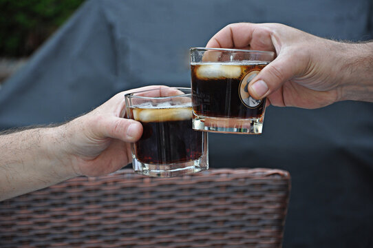 M&auml;nner H&auml;nde prosten mit Whiskey Gl&auml;ser gef&uuml;llt mit Mixgetr&auml;nk und Eisw&uuml;rfel, close up.